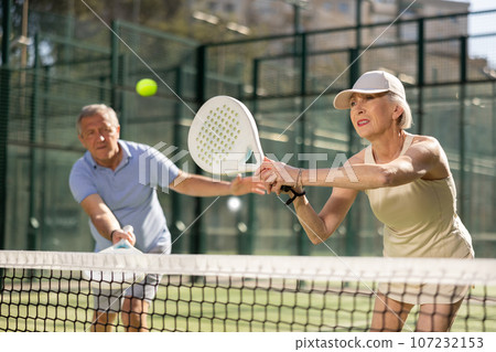 Motivated senior man and woman playing padel with his teammate in court 107232153