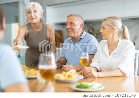Happy carefree older man and women gathering around kitchen table 107232179