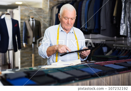 Experienced tailor looks at a pattern on a tablet screen in sewing atelier 107232192