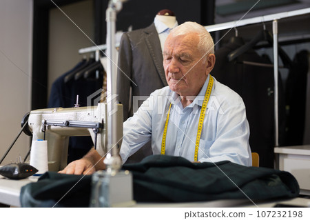 Portrait of elderly tailor working on sewing machine at studio 107232198