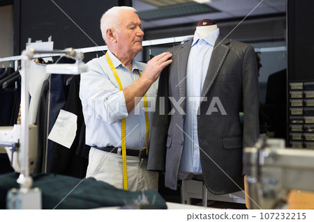 Experienced tailor threading jacket before starting work in workshop 107232215