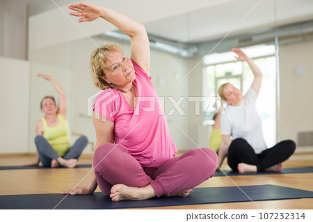 Women exercising during yoga class in fitness center - vakrasana pose Women exercising during yoga class in fitness center - vakrasana pose 107232314