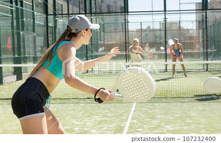 Young motivated woman playing padel with her teammate in court 107232400
