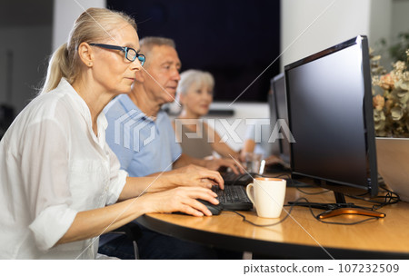 Focused senior woman in glasses attending group computer class Focused senior woman in glasses attending group computer class 107232509