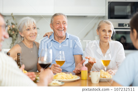 Old men and women talking merrily while having snack in the kitchen Old men and women talking merrily while having snack in the kitchen 107232511