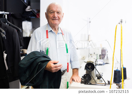Senior tailor posing next to sewing machine in sewing atelier 107232515