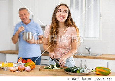 Happy elderly father and adult daughter preparing lunch together in modern kitchen Happy elderly father and adult daughter preparing lunch together in modern kitchen 107232532