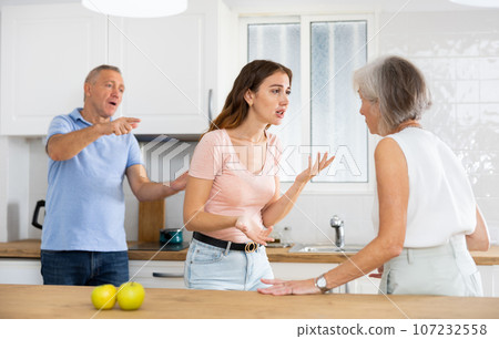 Quarrel between an elderly mother and an adult daughter in home kitchen. Father tries to calm everyone Quarrel between an elderly mother and an adult daughter in home kitchen. Father tries to calm everyone 107232558