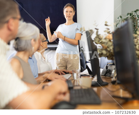 Middle-aged woman teacher speaking to mature attendees of computer courses 107232630