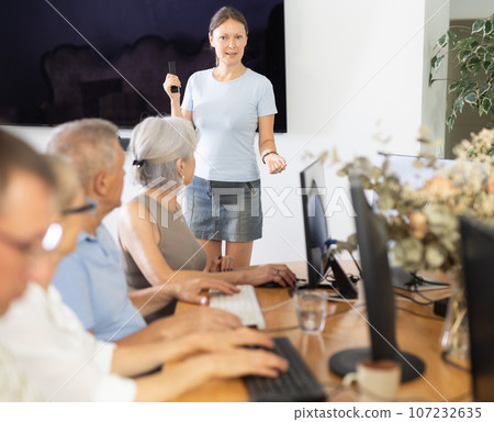 Middle-aged woman teacher speaking to mature attendees of computer courses Middle-aged woman teacher speaking to mature attendees of computer courses 107232635