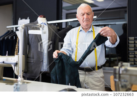 Professional tailor inspects mens jacket before starting work in workshop 107232663