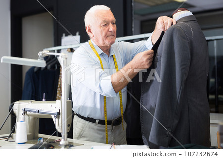 Experienced tailor tries on a new jacket on a mannequin in workshop Experienced tailor tries on a new jacket on a mannequin in workshop 107232674