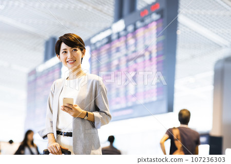A young businessman leaving for a business trip from the airport while looking at his smartphone A young businessman leaving for a business trip from the airport while looking at his smartphone 107236303