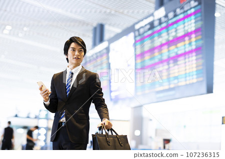 Young businessman on a business trip from the airport while looking at his smartphone 107236315