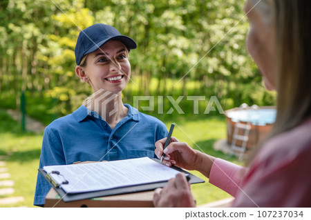 Courier delivering parcel, customer signs the delivery documents. 107237034