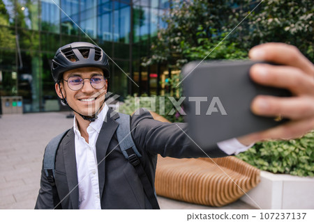 Smiling businessman in hemlet on a scooter making selfie 107237137