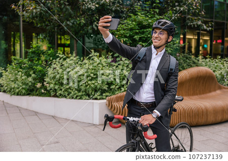 Smiling businessman in hemlet on a scooter making selfie Smiling businessman in hemlet on a scooter making selfie 107237139