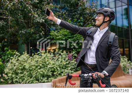 Smiling businessman in hemlet on a scooter making selfie Smiling businessman in hemlet on a scooter making selfie 107237140