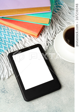 Composition with modern e-book reader, hardcover book and cup of coffee on table 107238348