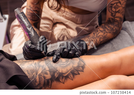 Professional tattoo master creating artistic masterpiece on female thigh Professional tattoo master creating artistic masterpiece on female thigh 107238414