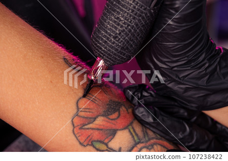 Tattoo machine in hands of professional master creating multicolored poppies Tattoo machine in hands of professional master creating multicolored poppies 107238422