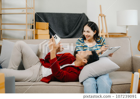 Asian young attractive couple man and woman use tablet and smartphone online shopping furniture decorate house with carton package move in new house. on sofa Asian young attractive couple man and woman use tablet and smartphone online shopping furniture decorate house with carton package move in new house. on sofa 107239091
