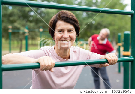 Elderly woman and a man do exercises on an open-air sports field 107239543