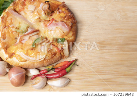 Pizza on wooden board with fresh peppers and basil with garlic on copy space background Pizza on wooden board with fresh peppers and basil with garlic on copy space background 107239648