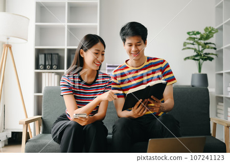 Two asian students learning together online with a laptop, tablet and tutor together in living room . 107241123