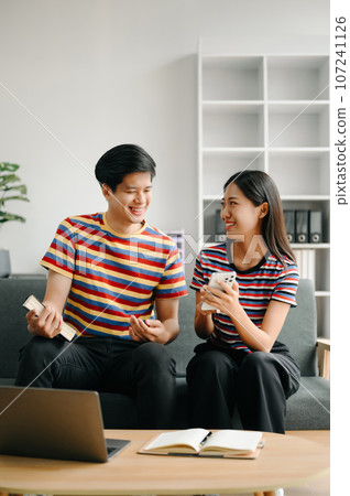 Two asian students learning together online with a laptop, tablet and tutor together in living room . 107241126