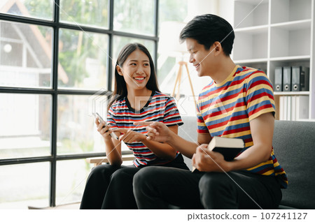 Two asian students learning together online with a laptop, tablet and tutor together in living room . 107241127