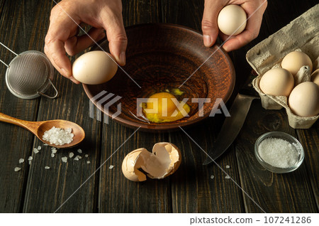 The process of cooking or frying eggs in the kitchen. The cook prepares eggs on the kitchen table for an omelette 107241286