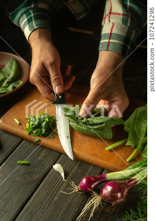 Slicing spinach with a knife on a cutting board. Cooking vegetable salad in the kitchen by the hands of a cook. The idea of a vegetarian diet 107241296