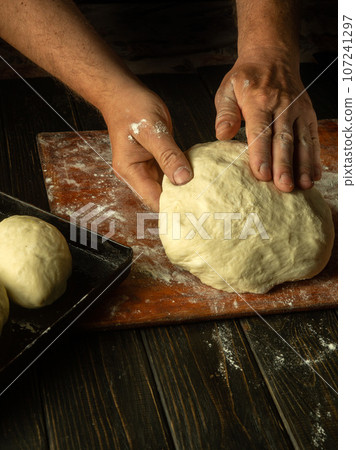 Close-up of a male baker's hands kneading dough on a kitchen board with flour powder. The concept of baking and confectionery 107241297