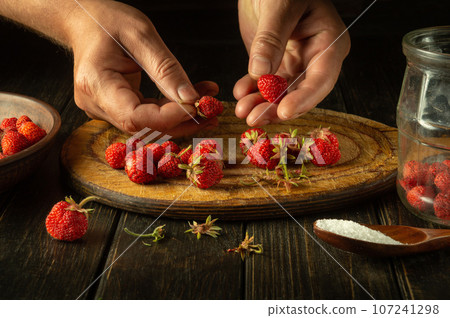 The chef prepares a drink from strawberries in a jar in the kitchen. Cleaning and sorting fragaria berries before filling with dill and adding sugar 107241298