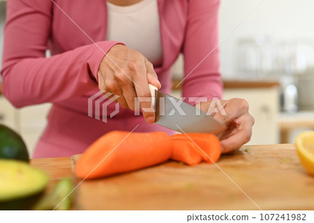 Sporty woman cutting fresh carrots, preparing healthy vegetables meal in kitchen. Dieting, healthy eating concept 107241982