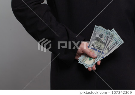 Businessman holding hiding money behind his back. Business person with US dollar cash money banknote Businessman holding hiding money behind his back. Business person with US dollar cash money banknote 107242369