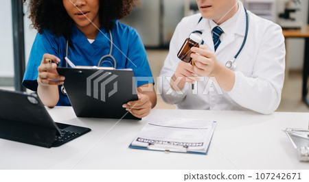Doctor Talks With Professional Head Nurse or Surgeon, They Use Digital tablet Computer. Diverse Team of Health Care Specialists Discussing Test Result on desk in hospital . 107242671