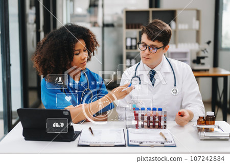 Doctor Talks With Professional Head Nurse or Surgeon, They Use Digital tablet Computer. Diverse Team of Health Care Specialists Discussing Test Result on desk 107242884
