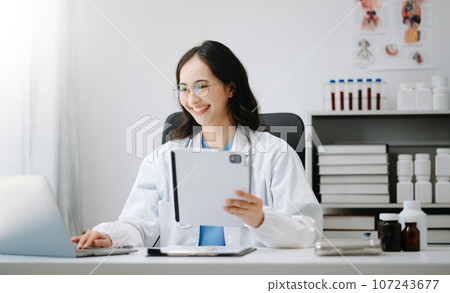 Beautiful physician doctor sit on table in office hospital. Attractive therapist female practitioner pharmacist smile and use tablet and laptop. after success work from treatment 107243677