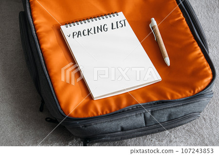 Travel Packing List For Vacation. Travel Packing Checklist For Holiday Or Business Trip. Open notepad with handwritten text Packing list in orange suitcase on bed at home Travel Packing List For Vacation. Travel Packing Checklist For Holiday Or Business Trip. Open notepad with handwritten text Packing list in orange suitcase on bed at home 107243853
