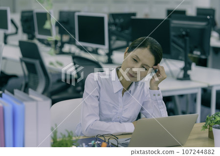 Middle-aged woman holding her temples in the office Middle-aged woman holding her temples in the office 107244882