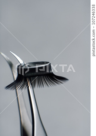 Close-up image of metal tweezers with eyelashes for extension on gray background. Concept of beauty. Beauty salon. 107246338
