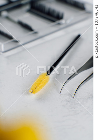Makeup artist's tools for eyelash extension tweezers, brush for combing yellow color lie on light background. MOCKUP. 107246343