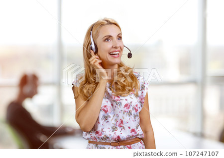 Portrait of smiling blondie wearing headset in office. Female customer support operator. Portrait of smiling blondie wearing headset in office. Female customer support operator. 107247107