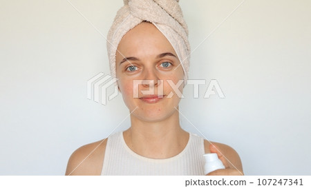 Cosmetic skincare routine. Health and beauty procedures. Smooth and clear skin. Wellness for face. Charming woman wrapped in bath towel holding bottle lotion isolated over white background 107247341