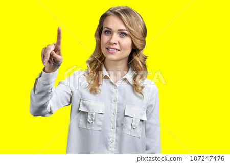 Portrait of blond woman is touching transparent virtual screen. Vivid yellow background. 107247476