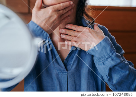 Senior woman checking wrinkles on her neck in the mirror Senior woman checking wrinkles on her neck in the mirror 107248095