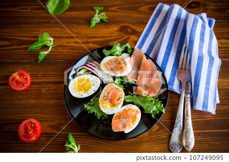 boiled eggs with salted red fish, herbs and seasonings in a plate . boiled eggs with salted red fish, herbs and seasonings in a plate . 107249095