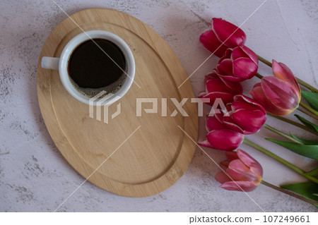 Cup of fresh coffee in white cup on wooden tray with beautiful pink tulip bouquet. Concept of morning holiday gift breakfast. Festive copy space Top view from above 107249661